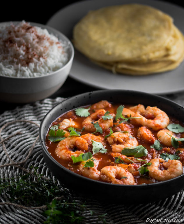 Prawn Rougaille served in a black bowl with rice and dhal puri in the background.