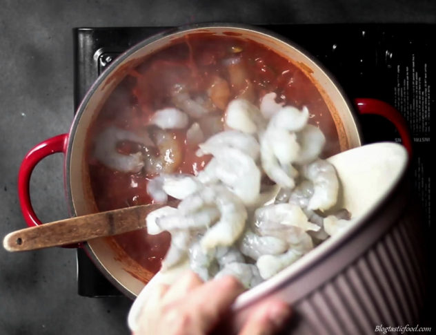 A photo of prawns being added to a tomato based spice mixture. 