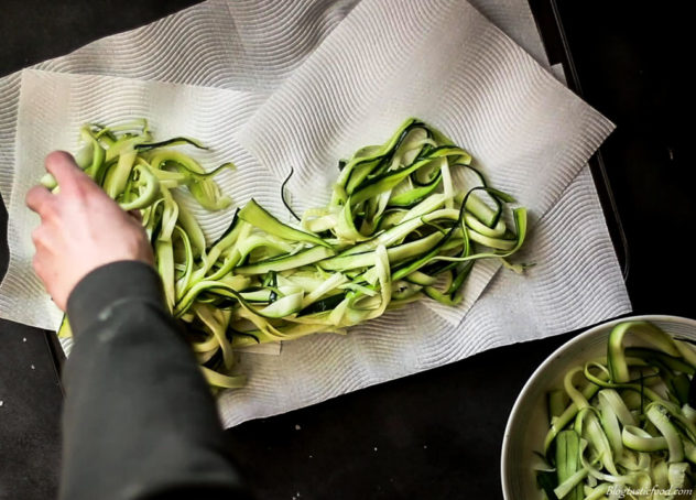 A photo of someone transfering zoodles from a bowl to a tray lined with kitchen paper.