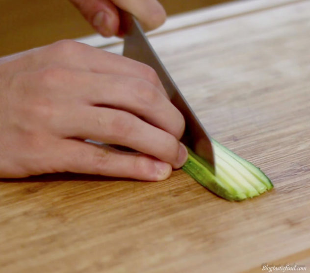 Someone using a knife to cut thin slithers of zucchini into zoodles.