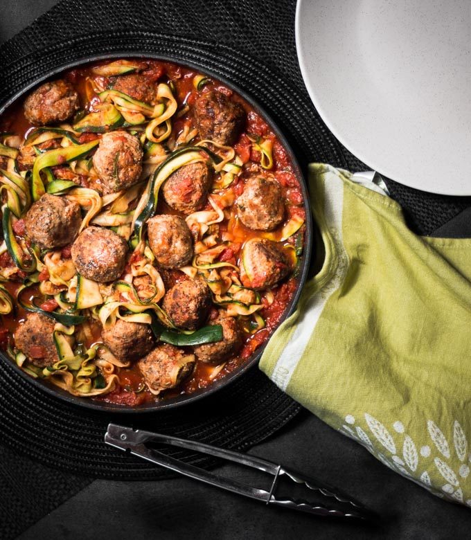 An overhead photo of a pan filled with zoodles and meatballs, surrounded by plate.