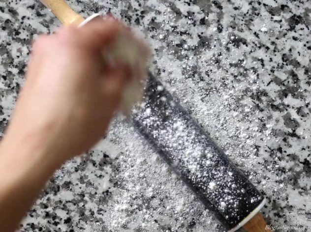 Someone using plain flour to lightly dust a surface and a rolling pin.