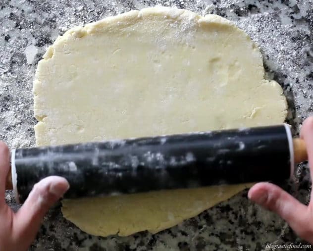 A photo of someone using a rolling pin to roll pastry on a flat surface.