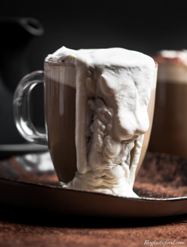 An eye level photo of a glass mug of baileys Irish coffee with cream spilling over the edge.