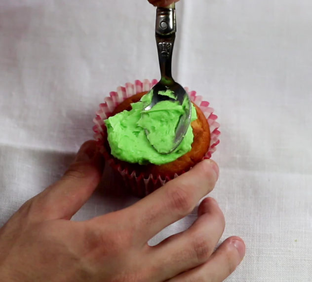 Green buttercream being spread over a cupcake.