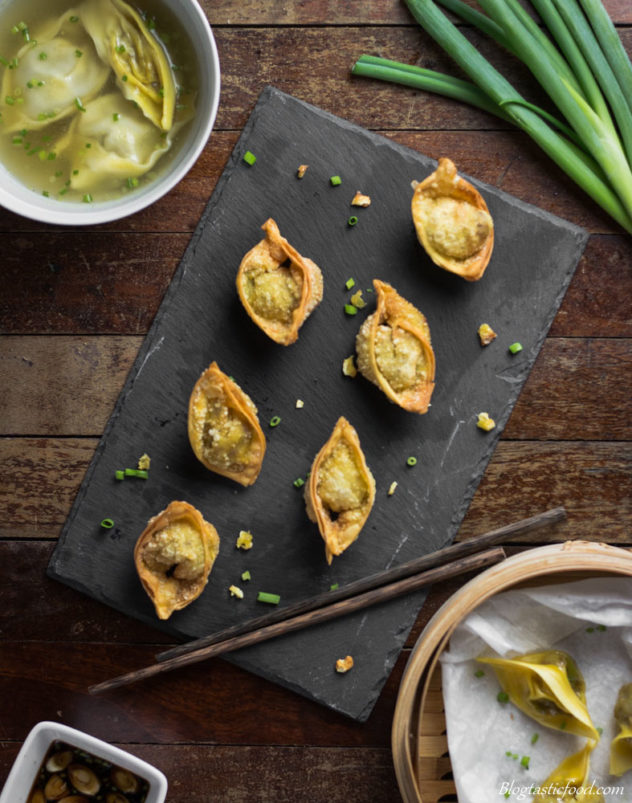 An overhead shot of 8 crispy deep fried wontons served on a sushi slate over a wooden suface.