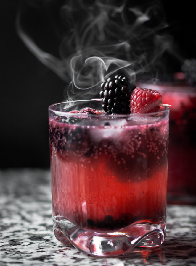 2 Black Widow themed cocktails on a granit surface with smoke rising above them.