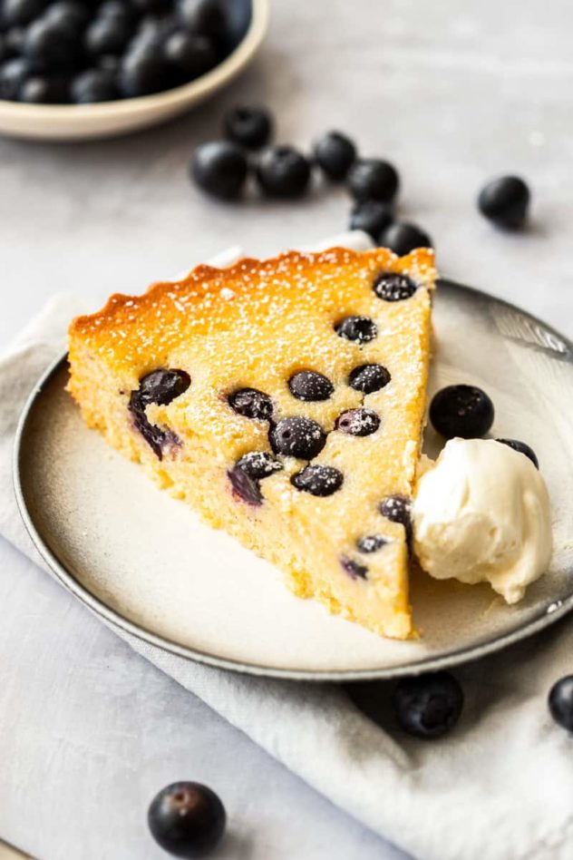 A portion of gluten free blueberry cake served on a white plate with a dark rim. 