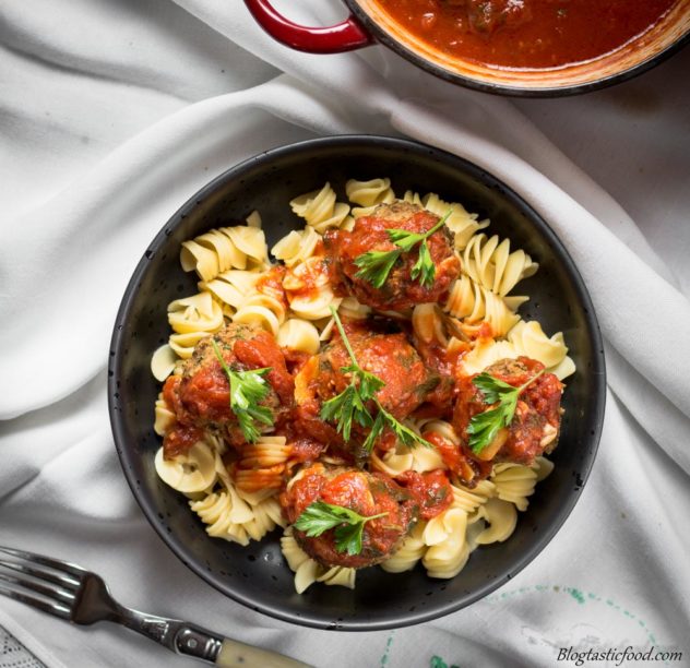 An overhead photo of lentil meatballs in a black bowl with pasta and tomato sauce.