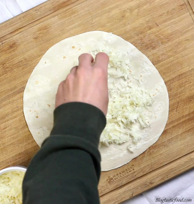 someone adding grated cheese on half of a tortilla.