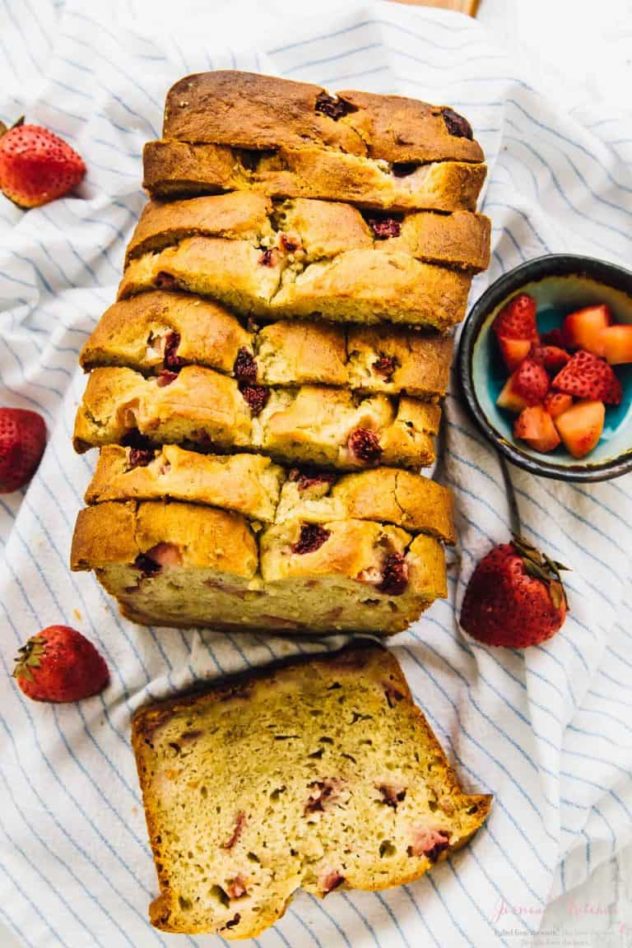 Strawberry banana bread sliced up on a white tea-towel, surrounded by fresh strawberries.