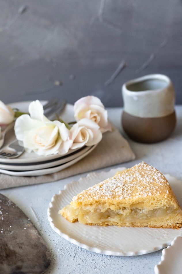 A portion of apple shortcake on a white plate, with white roses in the background.