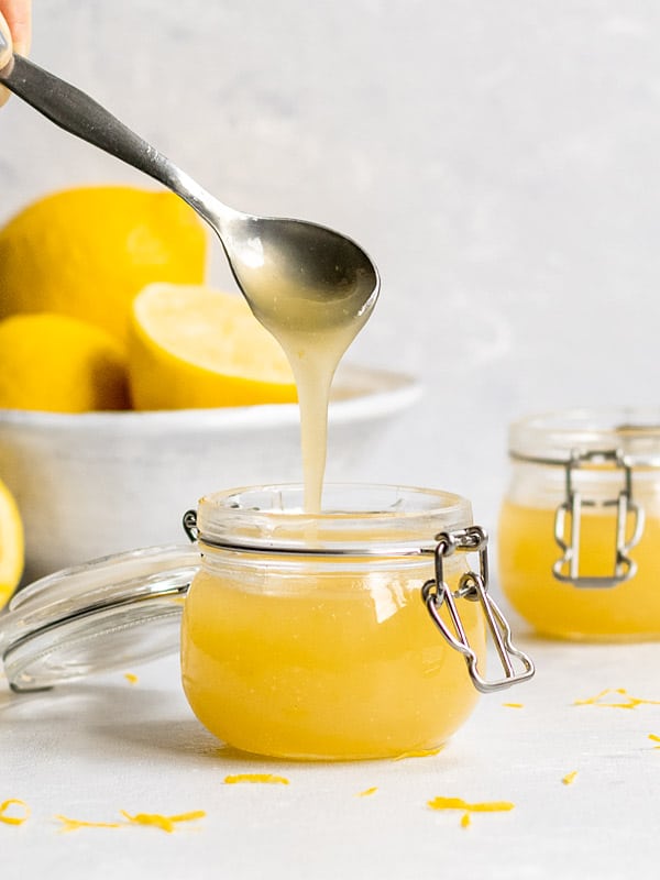 Vegan lemon curd drizzling off a spoon into a jar.