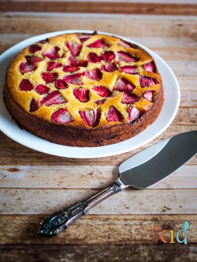 A strawberry, lemon and polenta cake served on a lrage white plate, beside a cake shovel.