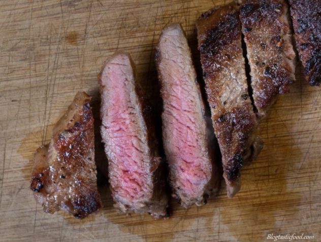 An overhead photo of sliced medium rare sirloin steak on a wooden board.