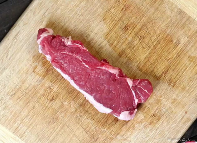 Raw sirloin steak on a wooden chopping board.