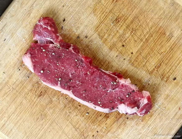 Raw sirloin steak that has been seasoned with salt and pepper.