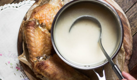A pot of turkey gravy with a ladle in it, and roastey turkey wings beside it.