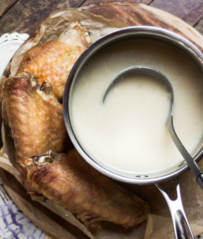A pot of turkey gravy with a ladle in it, and roastey turkey wings beside it.