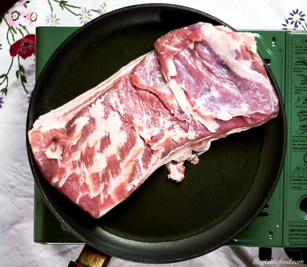A photo of pork belly searing in a pan skin side down.