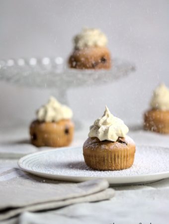 4 banana and chocolate chip muffins in a white tablecloth with icing sugar being dusted on top.