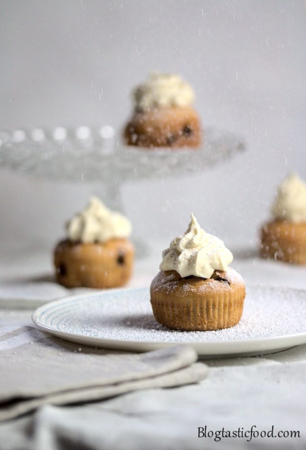 4 banana and chocolate chip muffins in a white tablecloth with icing sugar being dusted on top.