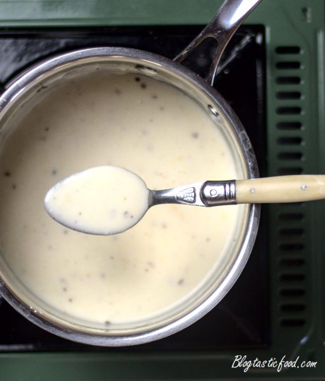 Sour cream sauce in a spoon, which is over a pot flled with the same sauce.
