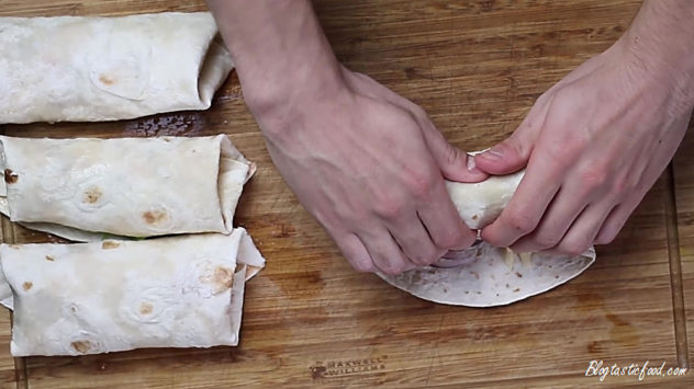 An enchilada being rolled up beside 3 other enchiladas.